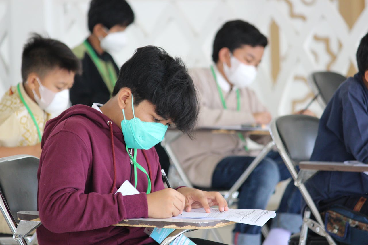 hero-services Teenagers wearing masks sit for an exam in an indoor setting, highlighting safety protocols.