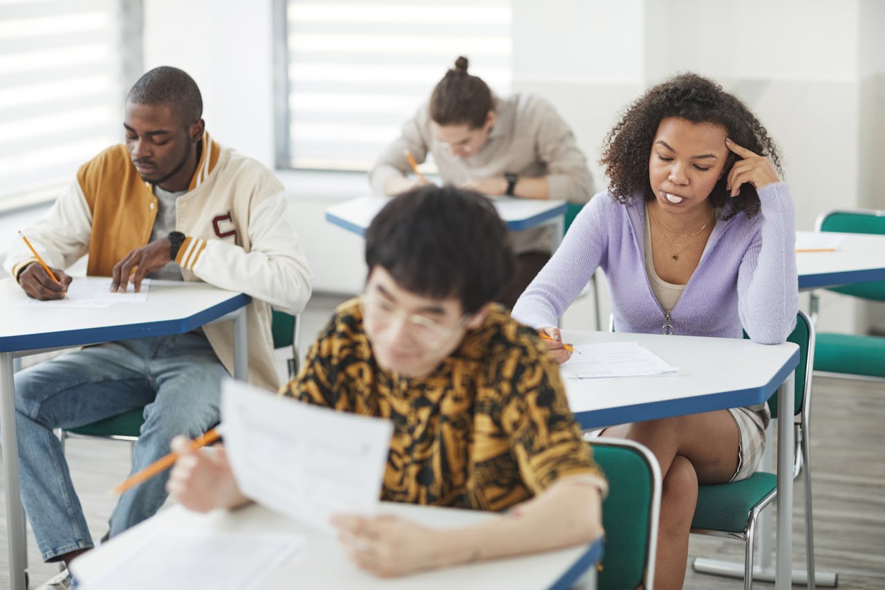 Students of various backgrounds focused on an exam in a bright, modern classroom setting.
